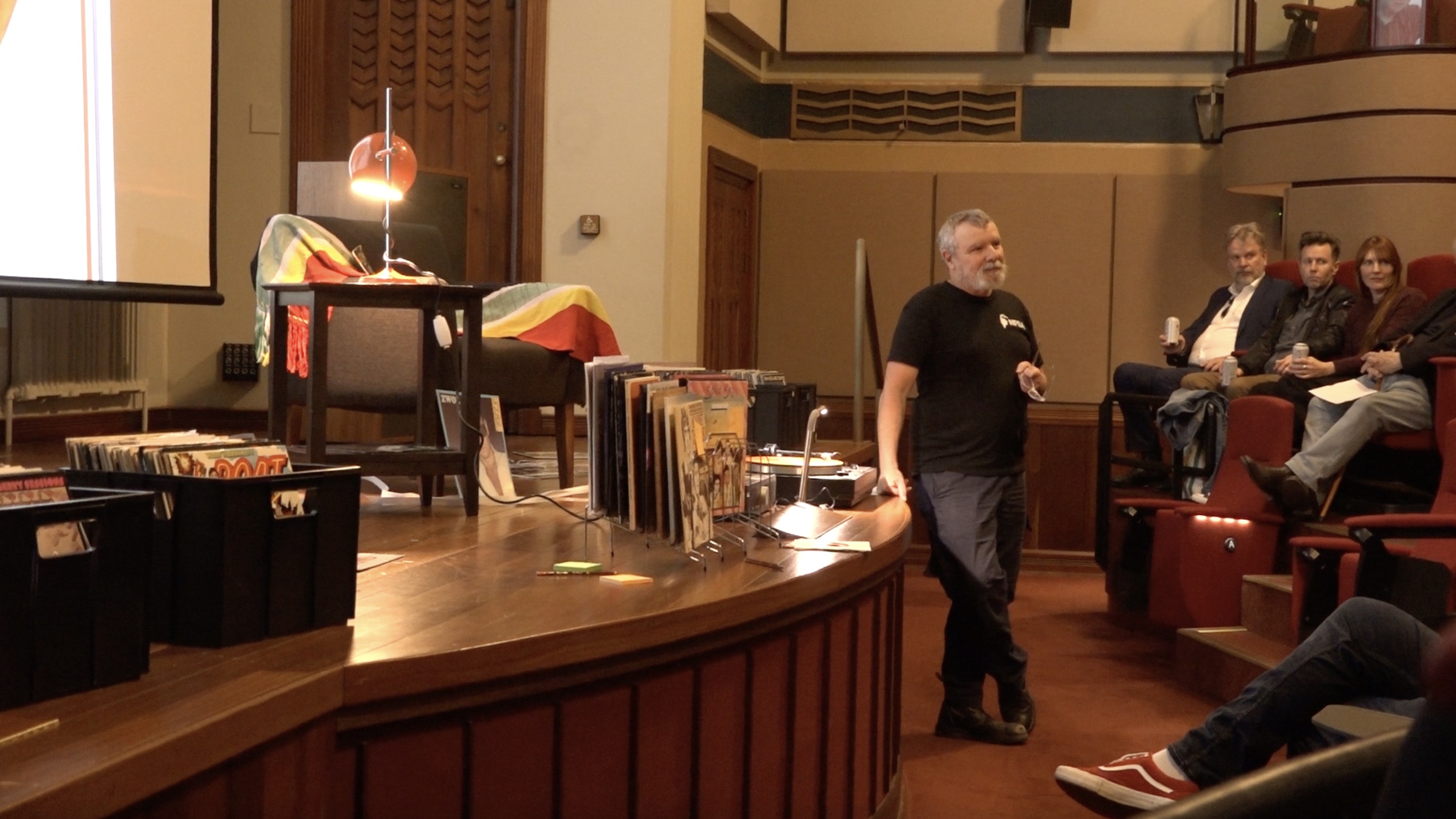 Thorsten leans up against a stage and looks out at a crowd. Behind him are vinyls.