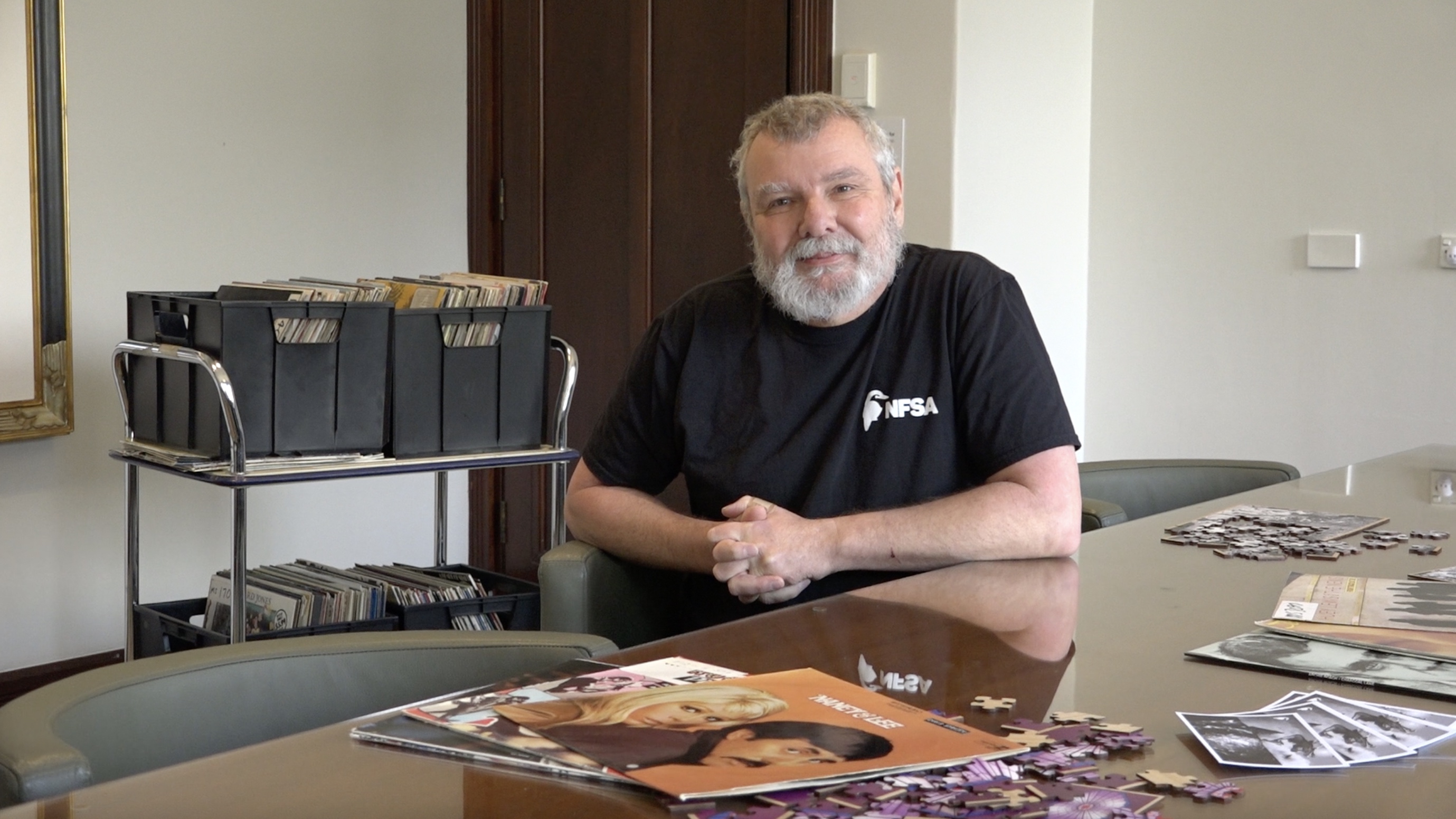 Thorsten Kaeding sits at a table with vinyls surrounding him. Behind him is a trolley with crates of old vinyls.