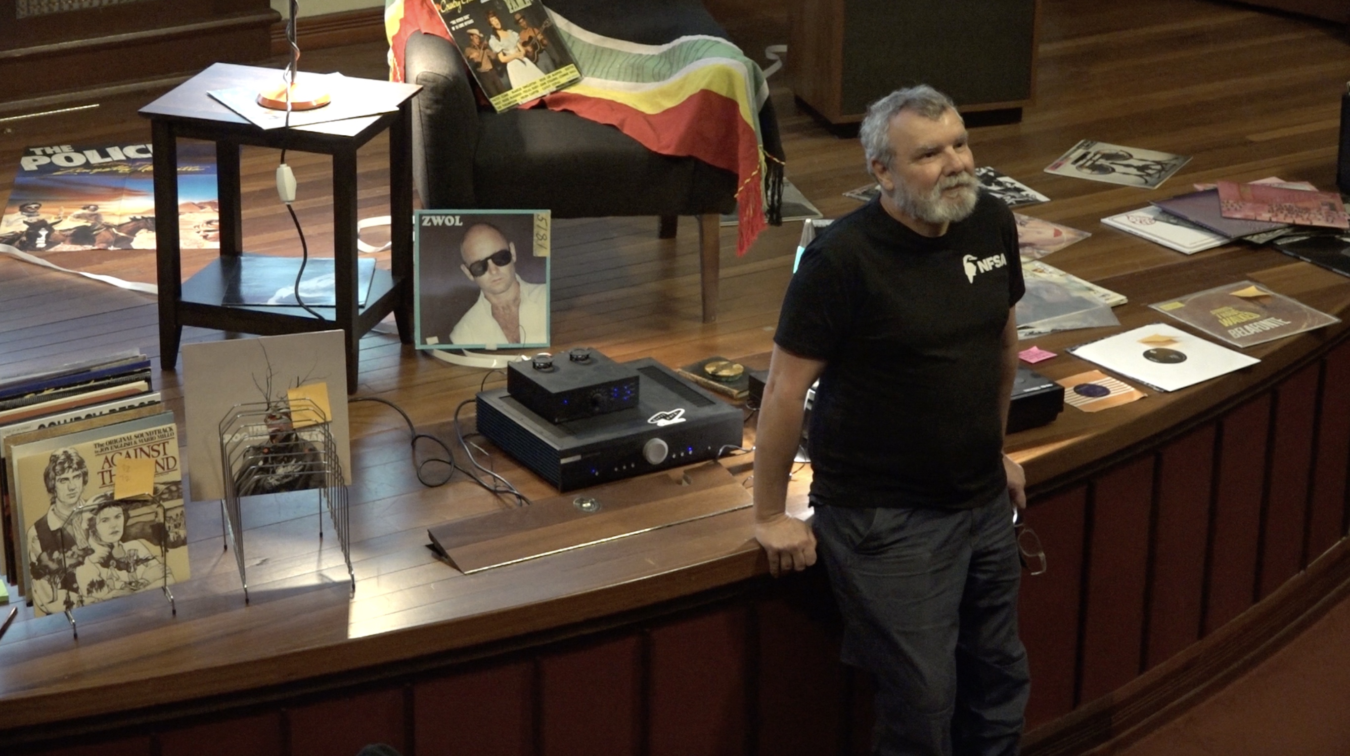 Thorsten leans up against the stage looking up at the crowd. He is listening to something. Behind him there are record sleeves and records on display