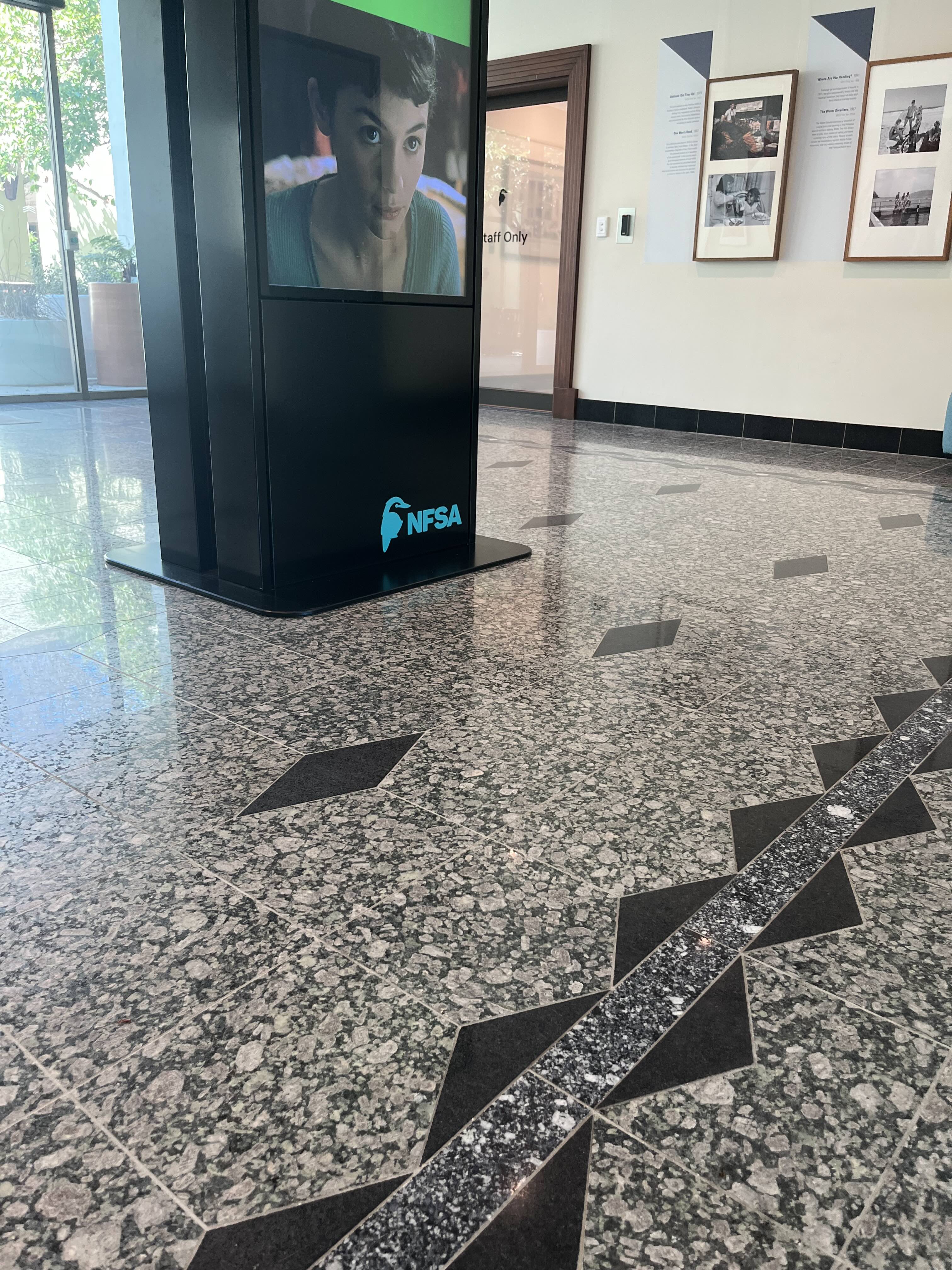 Dotted quartz floor underneath an electronic poster with a womens face on it.