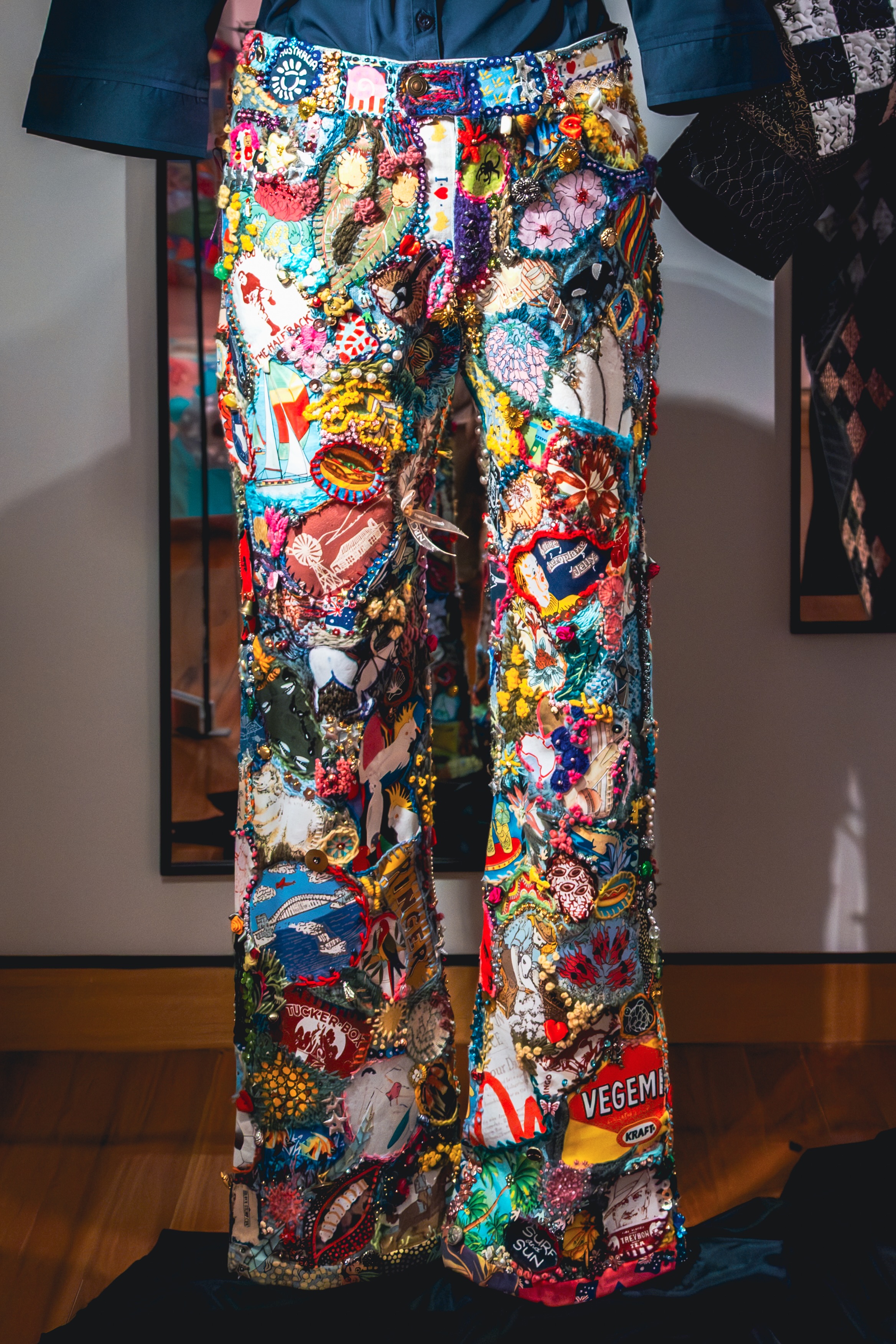 A pair of jeans covered with numerous patchwork items. They are colourful and many are themed to Australian culture.