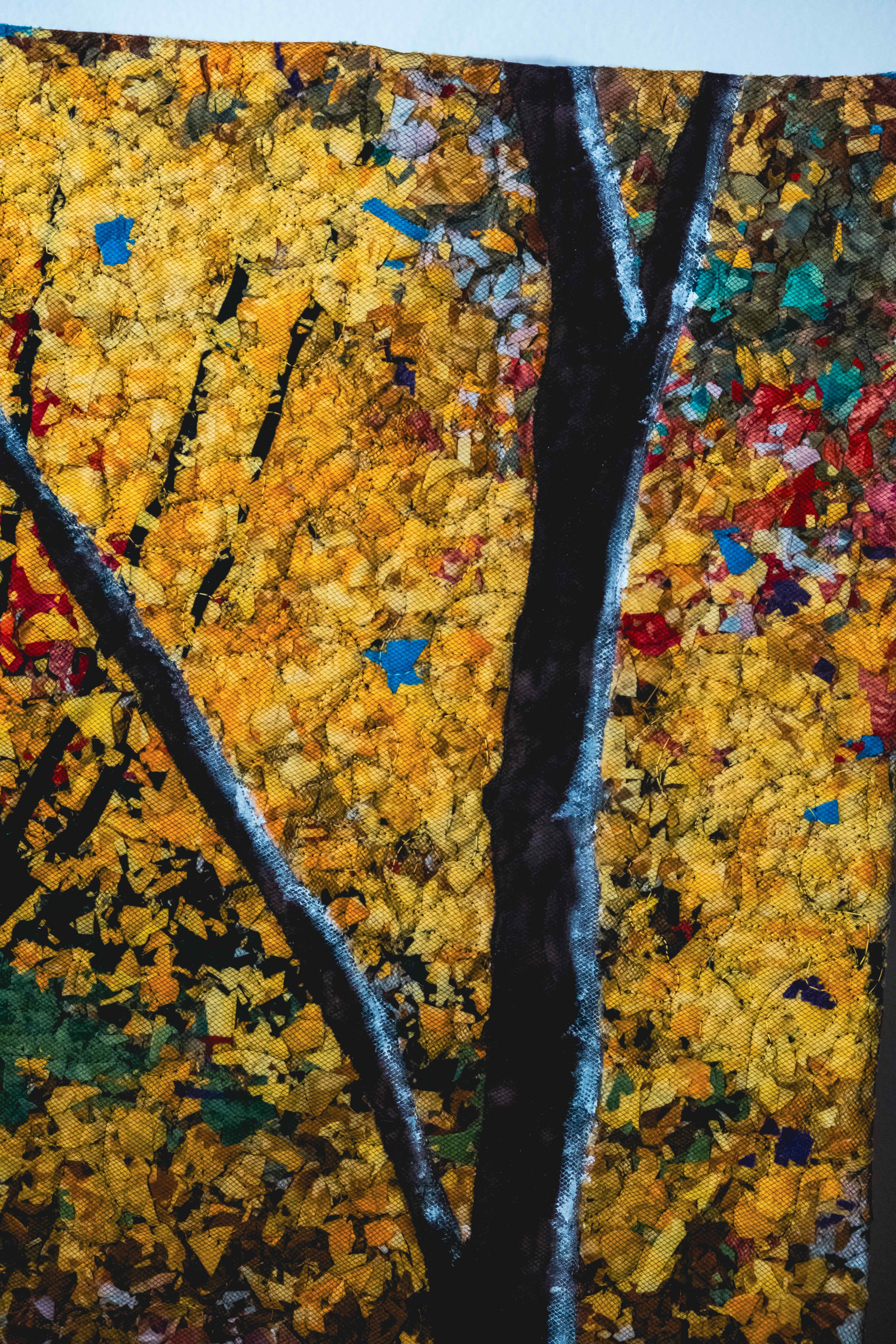 A small quilt with a tree design surrounded with yellow leaves. Tulle is stitched over the quilt.