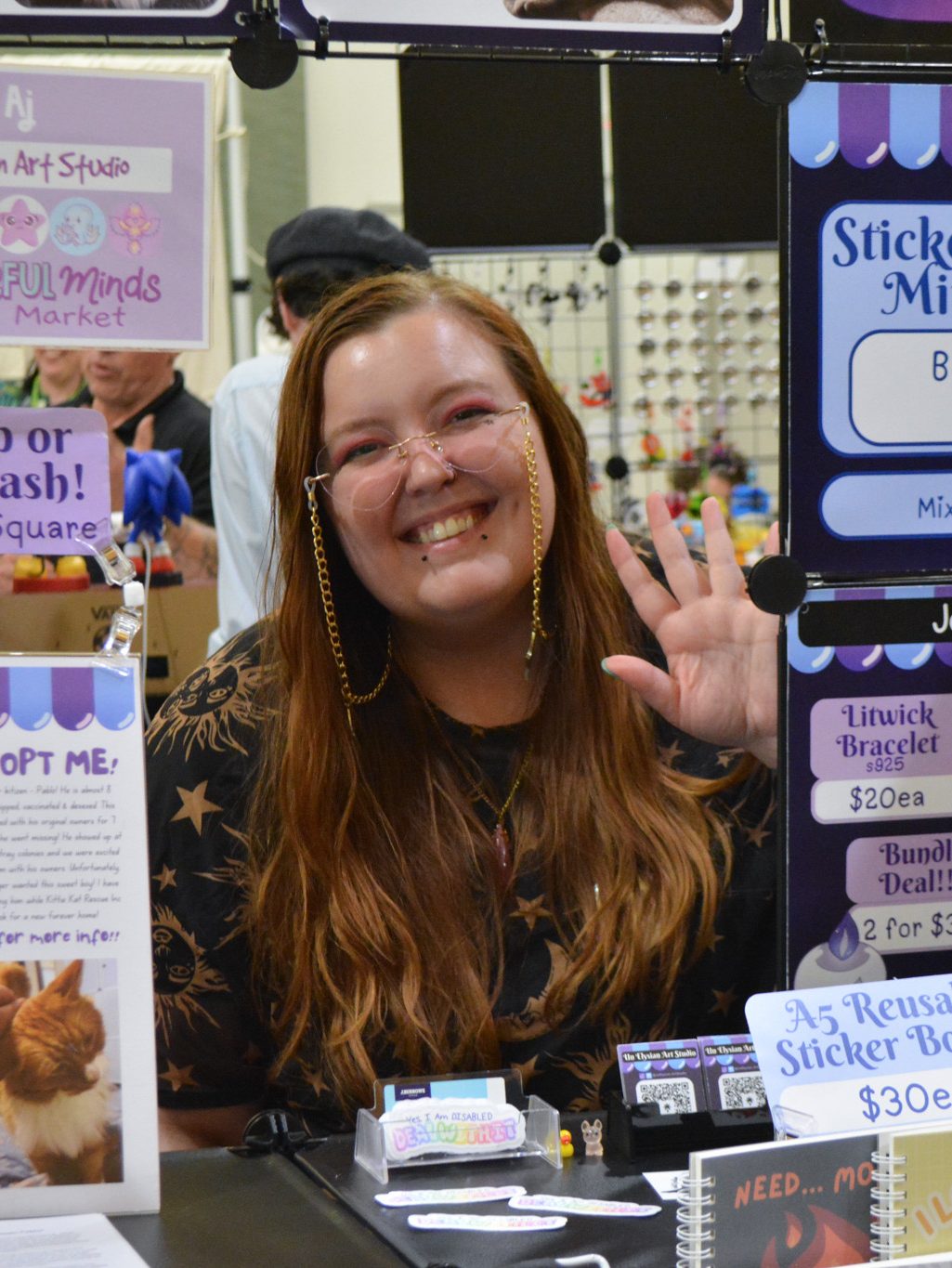 AJ seated at her market stall, hand waving
