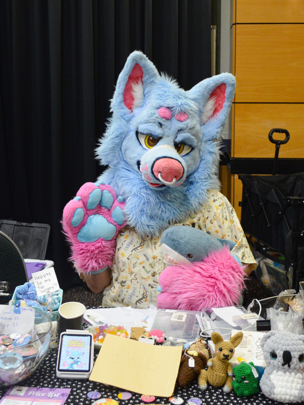 Parker seated at his market stall, wearing a blue and pink fur suit, paw waving