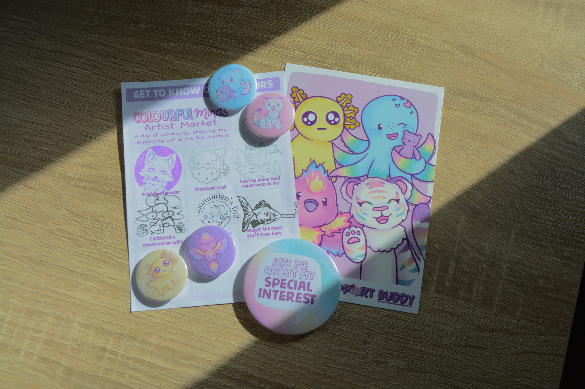 An arrangement of badges, a completed stamp sheet and a postcard from Colourful Minds