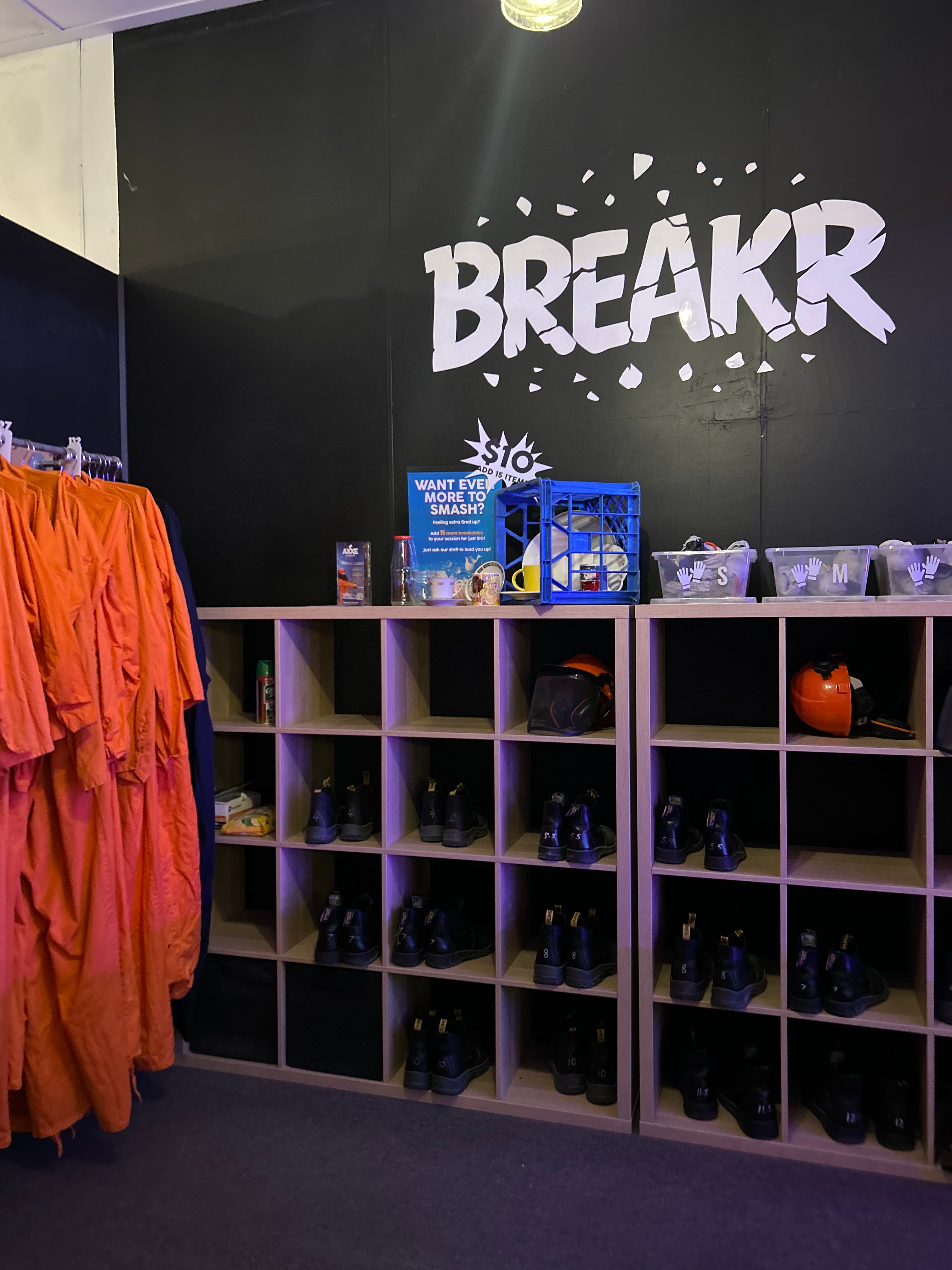 Orange jumpsuits, boots and protective headwear displayed for use in Breakr rage room