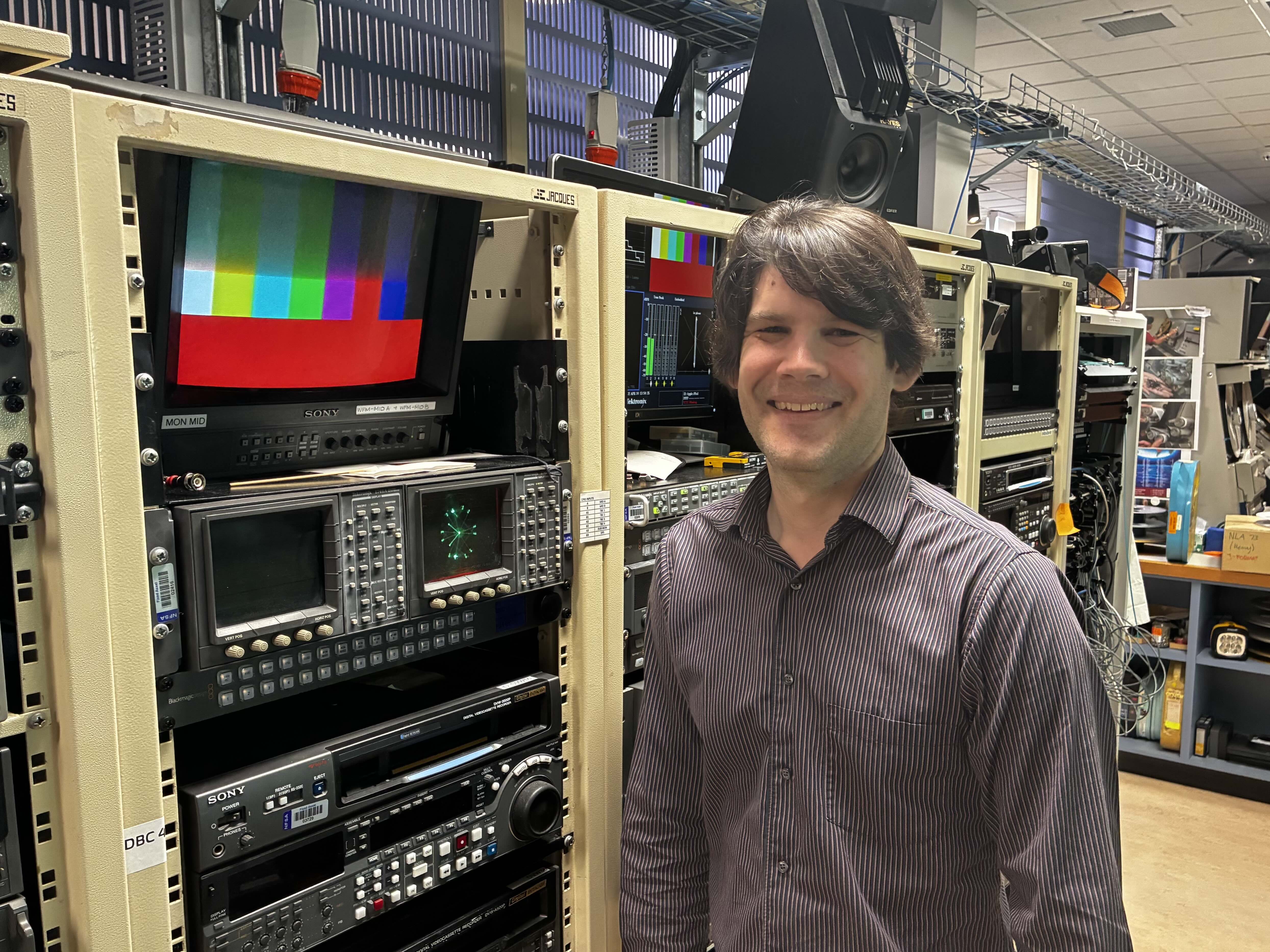 A man standing in front of a wall of  audio-visual equipment.