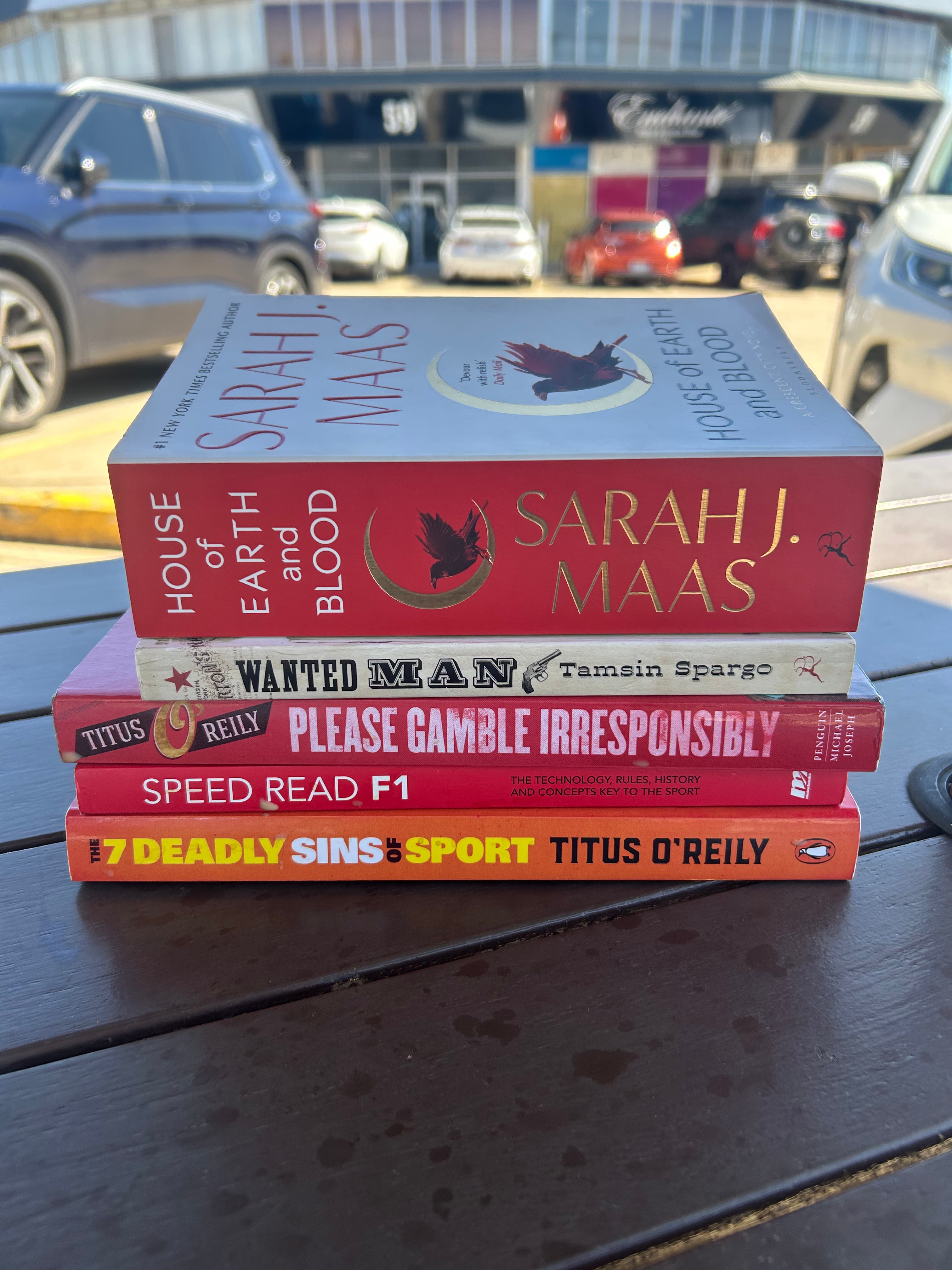 A stack of purchased books on a table outside.