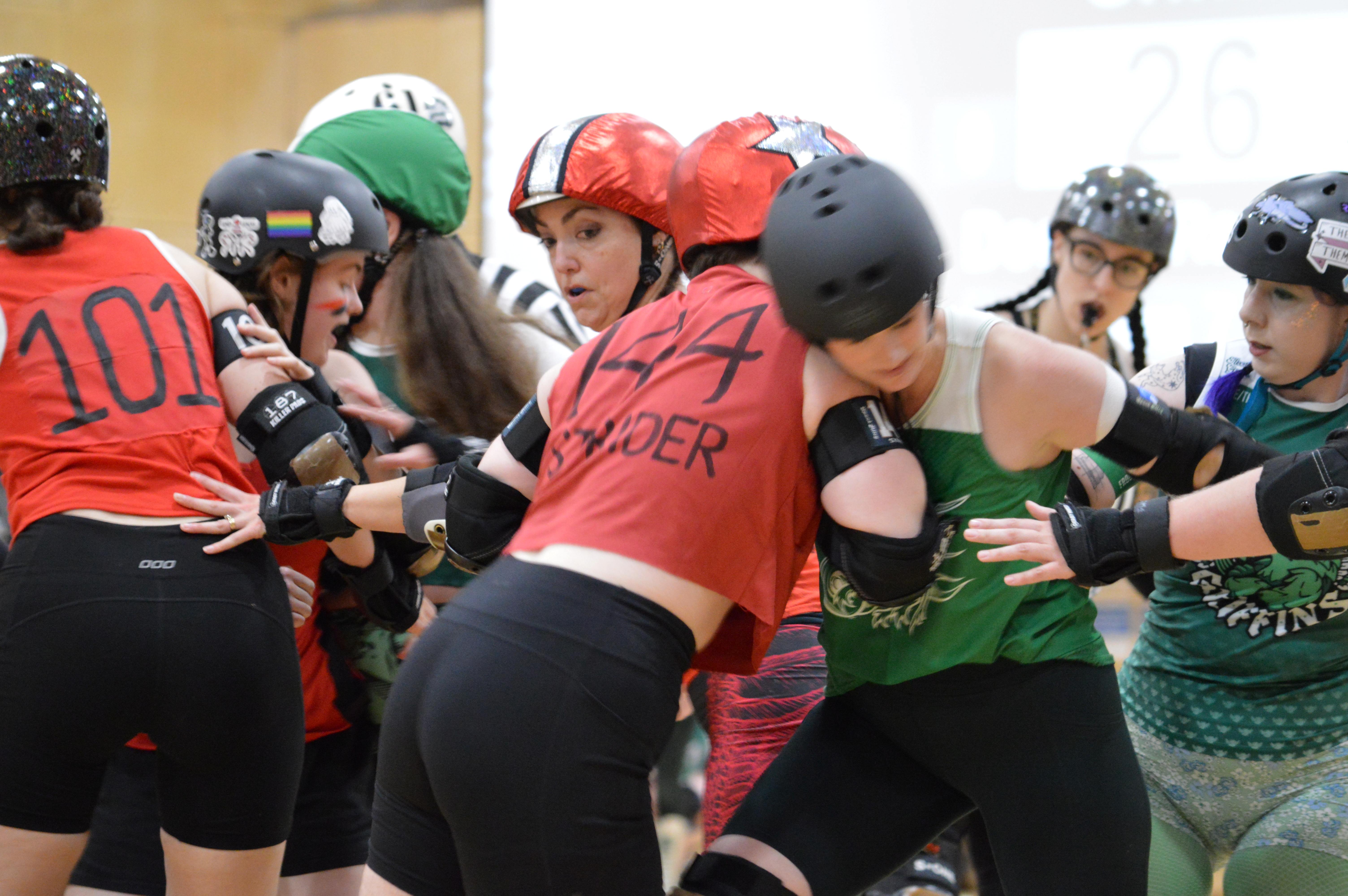 The jammer dressed in red is being blocked from passing a blocker in green.