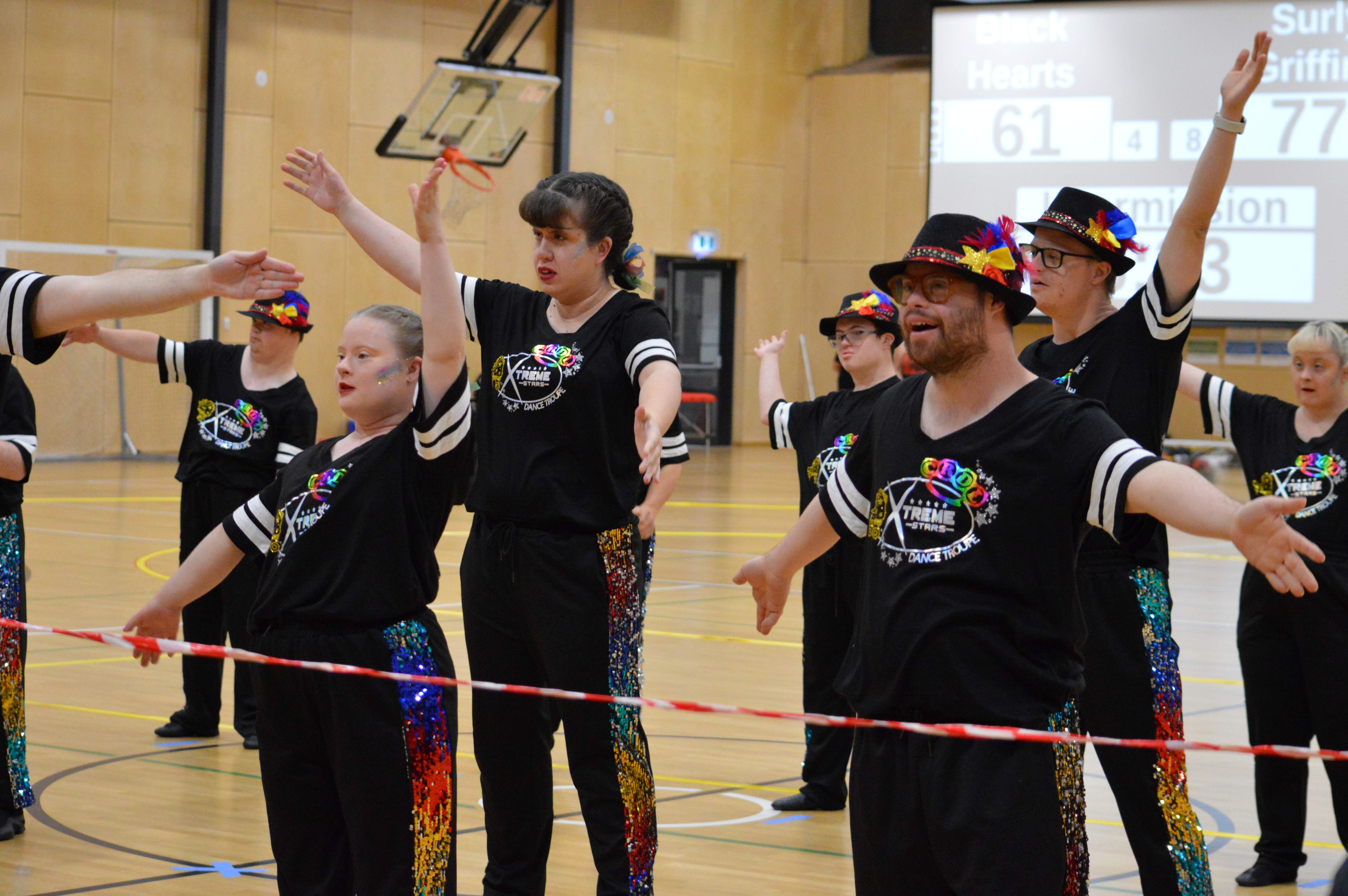 A group of dancers in shiny outfits dance behind the bollards keeping the audience off the stage/track.