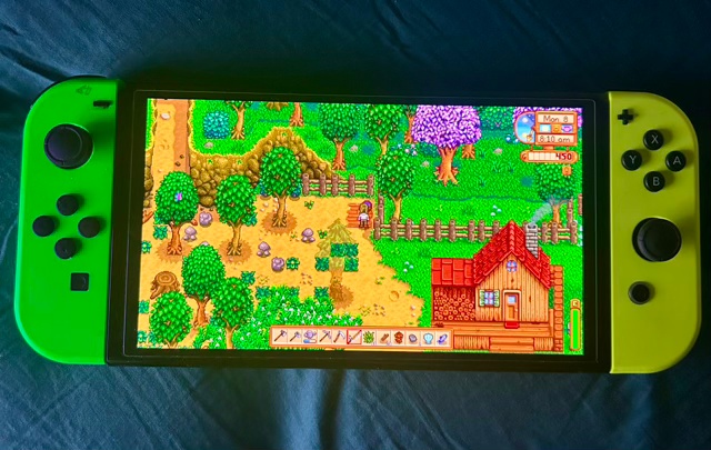 A Nintendo Switch with green controllers showing the farm in Stardew Valley