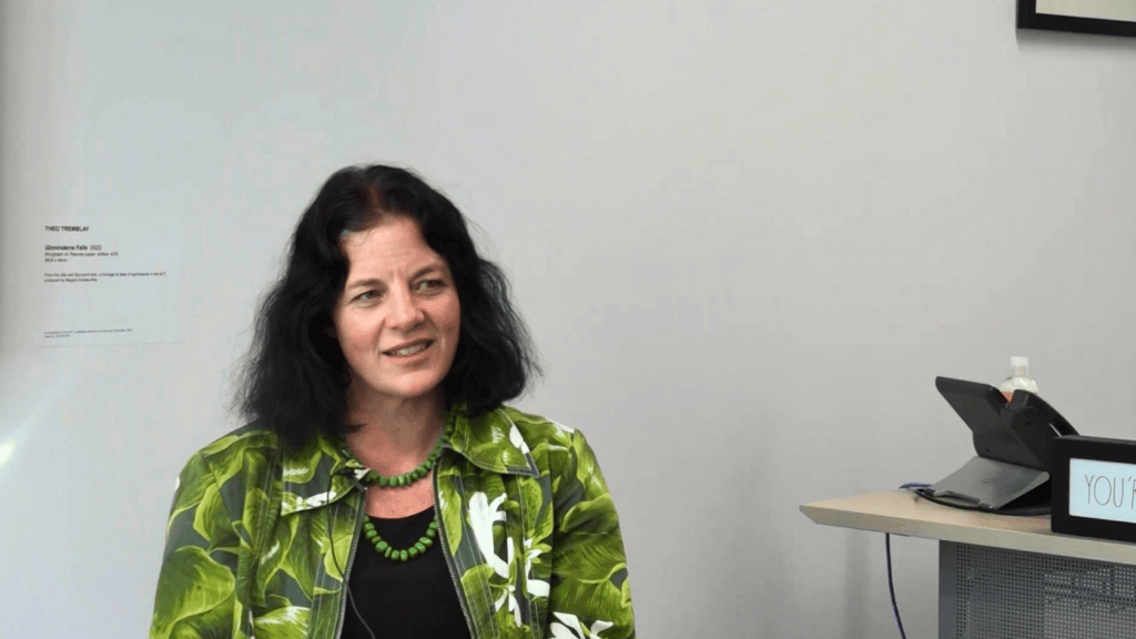 Landscape image of Jo Clay sitting in her office. She wears a jacket with green leaves on it.
